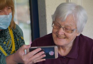 Older woman looking at something on a smart phone being held by a care worker